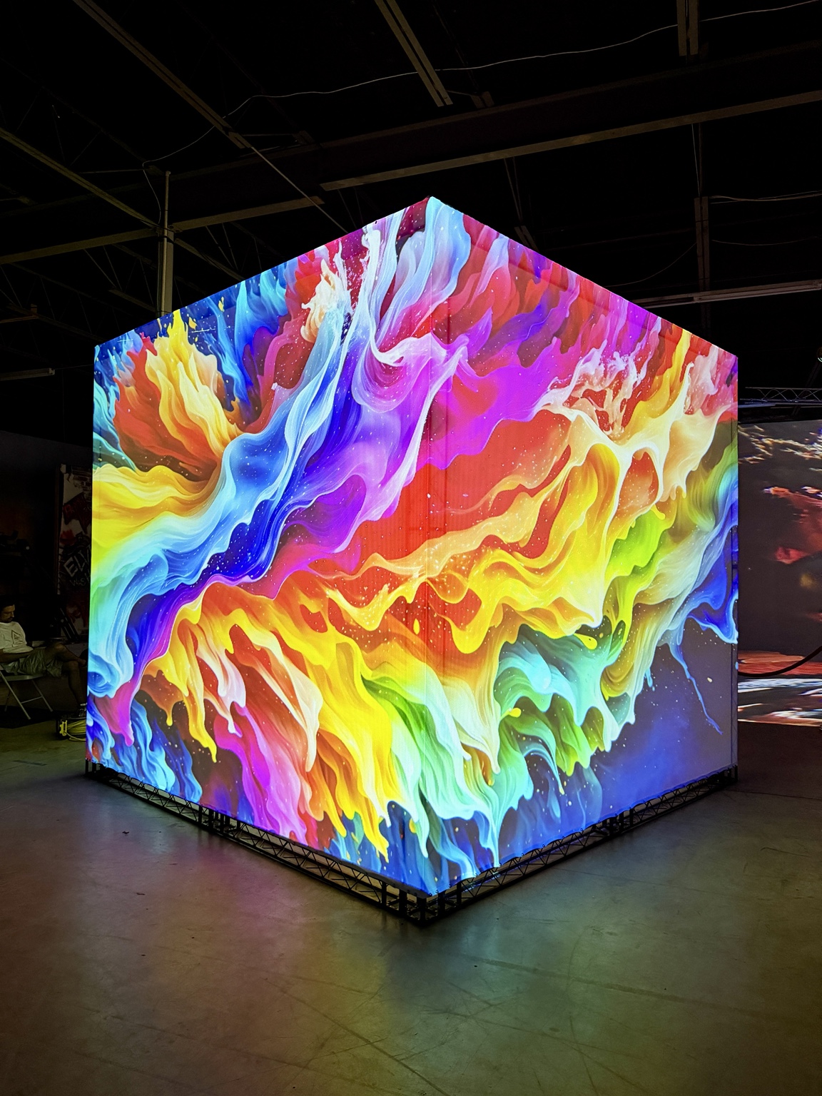 The Cube covered in flowing, multicolored projected artwork